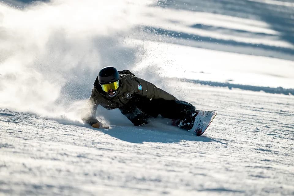 Snowboarder YES Academy in curva molto inclinata: la mano sfiora la neve battuta e alza una nuvola di neve