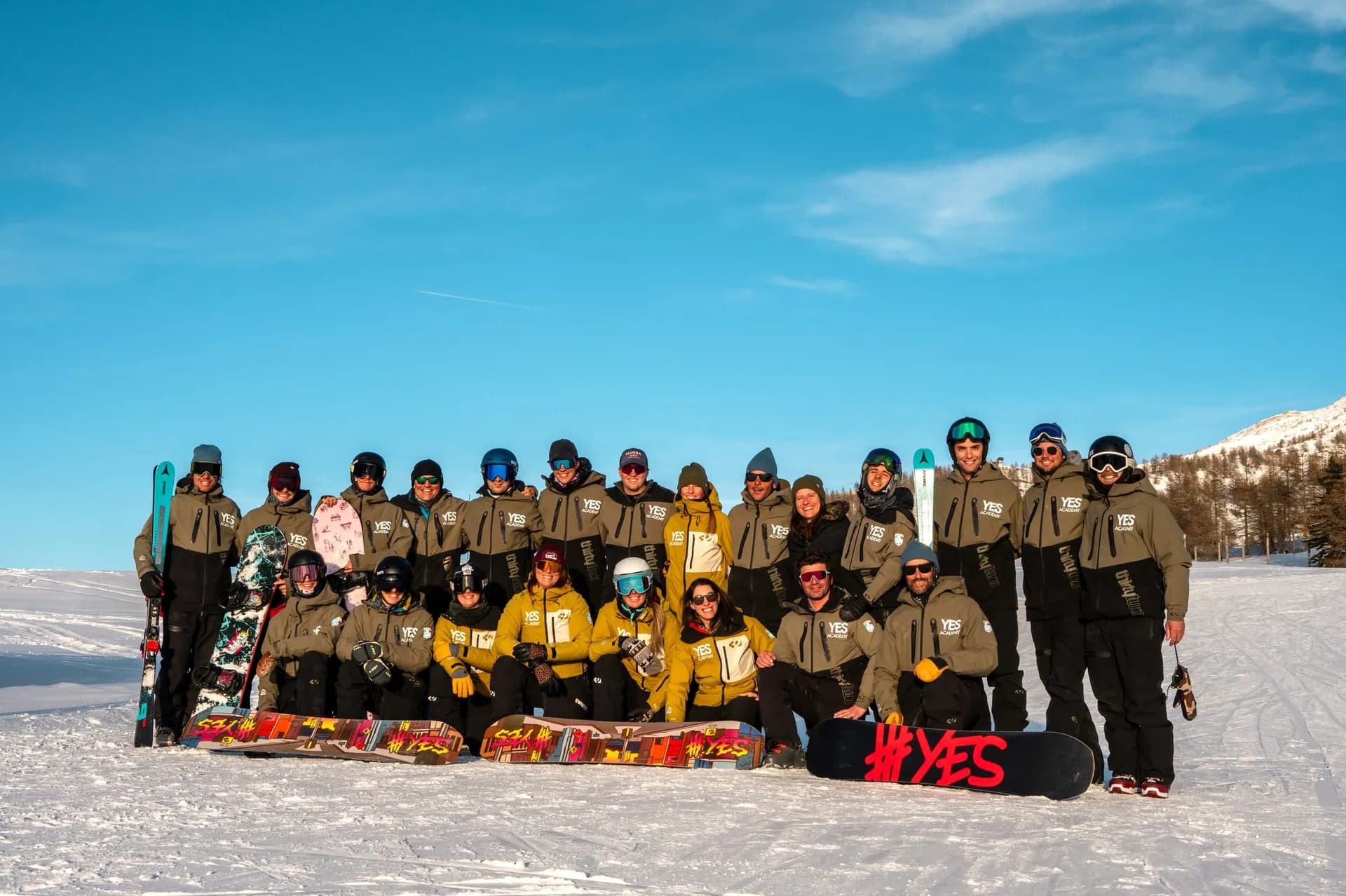 Foto di gruppo dei maestri YES Academy in divisa sulla neve, con sci e tavole, sotto un cielo blu