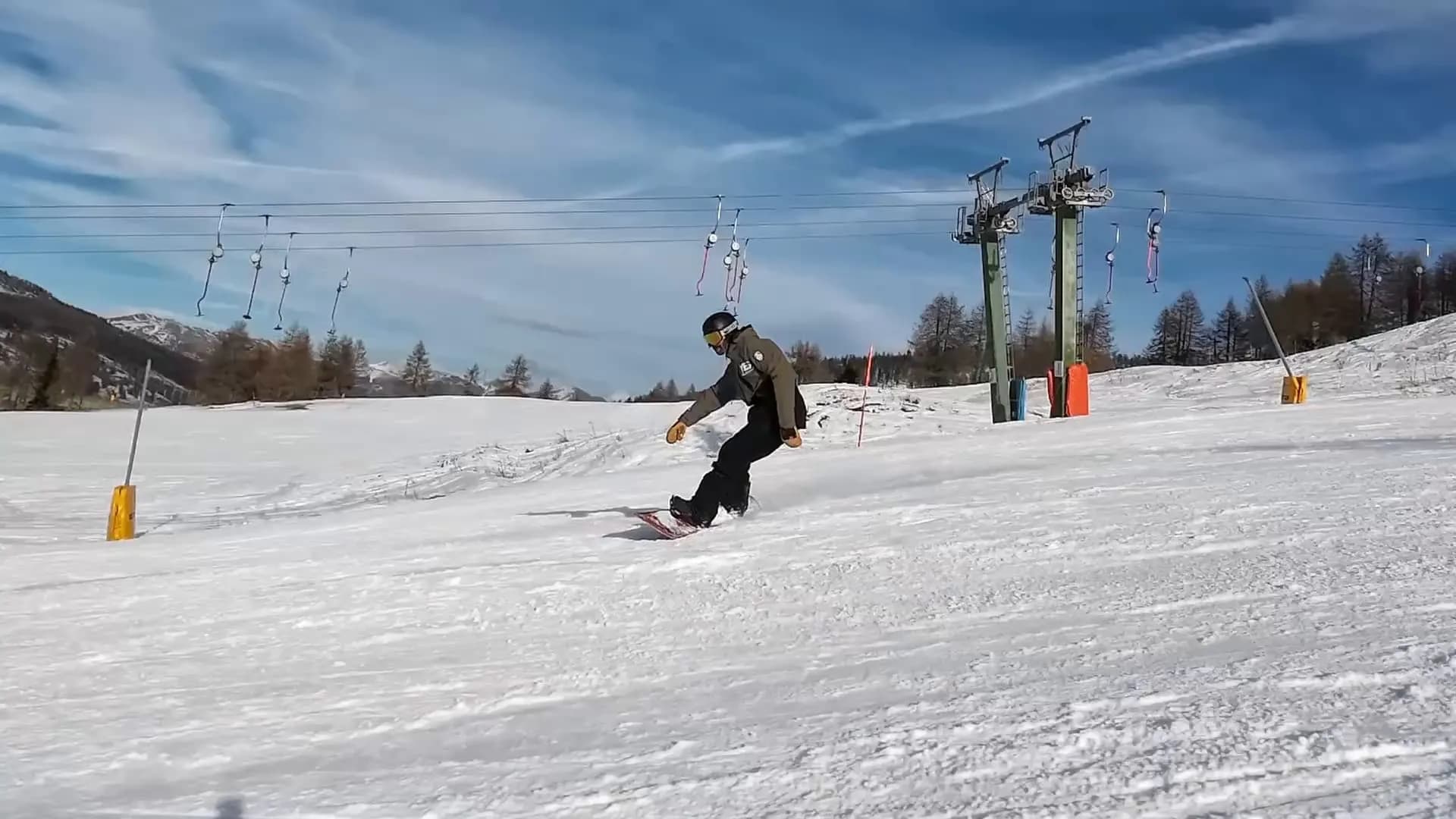 Snowboarder in curva su una pista di Sestriere, con skilift, larici e cielo blu sullo sfondo